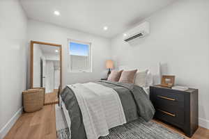 Bedroom featuring queen size bed, light wood-style flooring, a wall mounted air conditioner, and recessed lighting