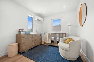 Bedroom with wood finished floors, a nursery area, recessed lighting, and a wall mounted AC