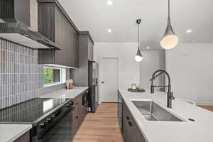 Kitchen featuring modern cabinets, wall chimney exhaust hood, light wood-type flooring, black stainless appliances, and pendant lighting