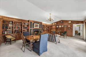 Carpeted dining area with lofted ceiling, wooden walls, and a chandelier