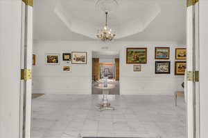 Hall with a decorative wall, wainscoting, a raised ceiling, ornamental molding, and marble finish flooring