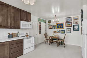 Kitchen with white appliances, light countertops, a chandelier, dark brown cabinetry, and decorative light fixtures