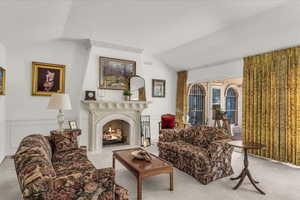 Sitting room with vaulted ceiling, a warm lit fireplace, and carpet flooring