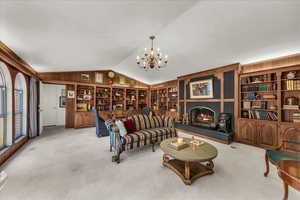 Carpeted living room featuring built in features, vaulted ceiling, a warm lit fireplace, a chandelier, and wooden walls