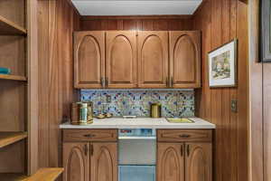Kitchen featuring open shelves, brown cabinets, wood walls, and light countertops