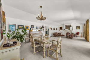 Dining space with a lit fireplace, lofted ceiling, light carpet, and a chandelier