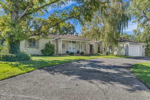 Ranch-style home with asphalt driveway, covered porch, a garage, and a front lawn