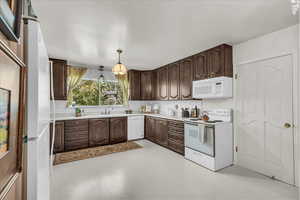 Kitchen featuring white appliances, backsplash, light countertops, and dark brown cabinets