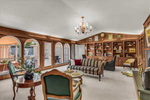 Carpeted living room featuring vaulted ceiling, wood walls, a chandelier, and built in shelves