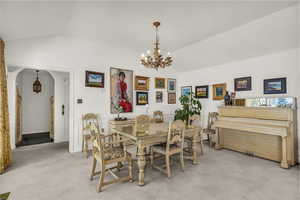 Dining room featuring arched walkways, light colored carpet, vaulted ceiling, and a chandelier