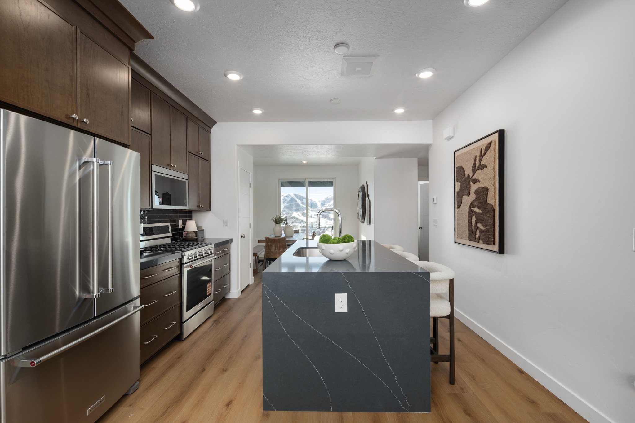 Kitchen with stainless steel appliances, dark wood finish cabinetry, a kitchen island with sink, light wood-type flooring, and a textured ceiling