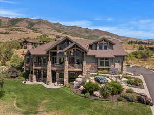 View of front of property with stone siding, a balcony, a mountain view, a chimney, and a front lawn