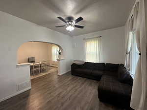 Living area with arched walkways, dark wood finished floors, and ceiling fan