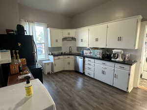 Kitchen featuring stainless steel appliances, dark wood finished floors, white cabinetry, and dark countertops