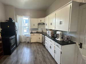 Kitchen featuring dark countertops, dark wood-type flooring, appliances with stainless steel finishes, and white cabinetry