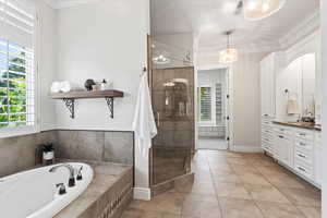 Full bathroom featuring ornamental molding, a bath, vanity, light tile patterned floors, and a stall shower