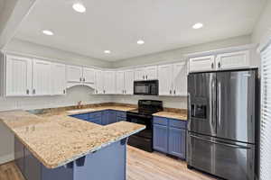 Kitchen with white cabinetry, black appliances, blue cabinetry, light stone countertops, and recessed lighting