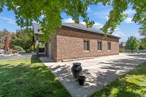 View of side of property with a yard, brick siding, a shingled roof, and a patio area