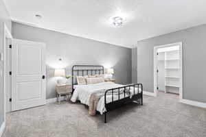 Bedroom featuring light colored carpet, a walk in closet, and a textured ceiling