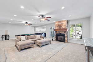 Living area with light colored carpet, a textured ceiling, ceiling fan, a stone fireplace, and recessed lighting