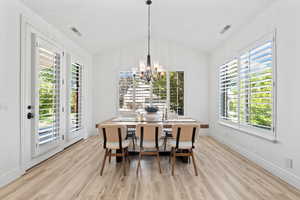 Dining area featuring a chandelier, lofted ceiling, light wood finished floors, and plenty of natural light