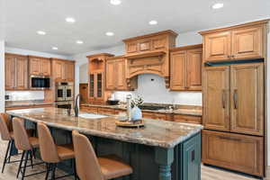 Kitchen with an island with sink, light stone countertops, recessed lighting, brown cabinets, and a textured ceiling