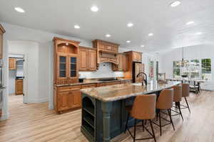 Kitchen with open shelves, brown cabinetry, recessed lighting, dark stone countertops, and a kitchen bar