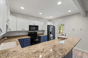 Kitchen featuring white cabinets, black appliances, light stone counters, light wood-type flooring, and blue cabinets