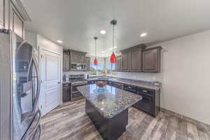 Kitchen with stainless steel appliances, dark stone counters, a kitchen island, hanging light fixtures, and a textured ceiling