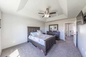 Bedroom featuring a tray ceiling, light colored carpet, and a ceiling fan