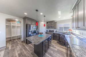 Kitchen with decorative light fixtures, stainless steel appliances, a center island, dark stone countertops, and light wood-type flooring