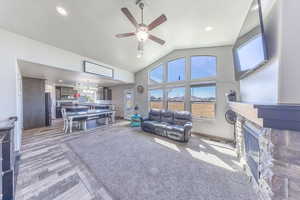 Living room with high vaulted ceiling, a fireplace, a ceiling fan, a chandelier, and light wood-style finished floors