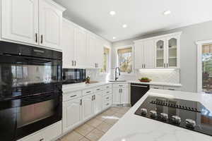 Kitchen featuring black appliances, white cabinetry, glass fronted cabinets, backsplash, and light stone countertops