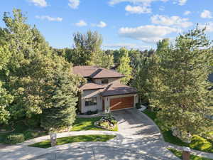 View of front of house featuring driveway, a forest view, stucco siding, roof with shingles, and an attached garage