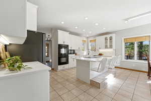 Kitchen featuring white cabinetry, light tile patterned floors, black appliances, a kitchen island, and glass insert cabinets