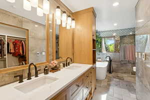 Full bathroom featuring a freestanding bath, tile walls, double vanity, a tile shower, and a walk in closet