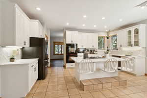 Kitchen with backsplash, recessed lighting, a breakfast bar, black appliances, and a kitchen island