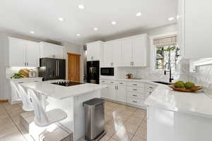 Kitchen featuring white cabinetry, light stone countertops, black appliances, recessed lighting, and a center island