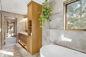 Bathroom featuring vanity, tile walls, and a freestanding bath