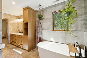 Full bath featuring tile walls, a freestanding tub, vanity, and recessed lighting