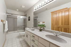 Bathroom with double vanity, bath / shower combo with glass door, and light tile patterned floors
