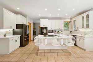 Kitchen featuring tasteful backsplash, a breakfast bar, recessed lighting, light tile patterned floors, and black appliances