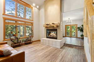 Living room with a towering ceiling, a tile fireplace, wood finished floors, and a chandelier