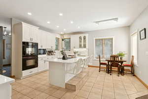 Kitchen featuring recessed lighting, black appliances, light tile patterned floors, a kitchen breakfast bar, and white cabinets