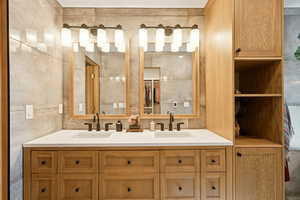Bathroom featuring double vanity, tile walls, and a spacious closet