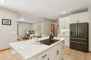 Kitchen with high end fridge, light tile patterned floors, white cabinets, tasteful backsplash, and a center island
