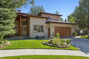 Prairie-style home with asphalt driveway, stucco siding, a garage, a front lawn, and a chimney
