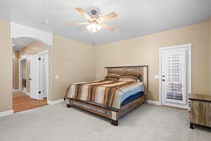 Bedroom featuring light colored carpet, ceiling fan, access to exterior, and arched walkways