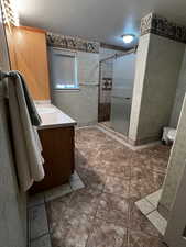 Full bathroom featuring a textured ceiling, vanity, a stall shower, and tile patterned floors