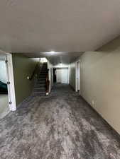 Finished basement area with gray colored carpet, stairs, and a textured ceiling